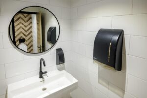Modern restroom with a white tiled wall, black fixtures, a rectangular sink, and a round mirror reflecting a chevron-patterned wall.